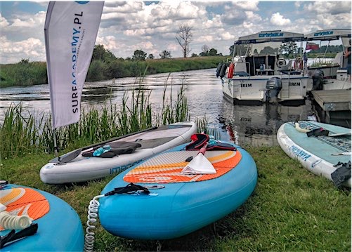 Supboards aan de kant van een rivier met vlag SUP Acadamy Poland.