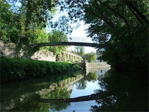 Een rustige waterweg in Arcachon, Frankrijk, met een sierlijke brug die het water overspant en oude stenen muren omgeven door weelderig groen