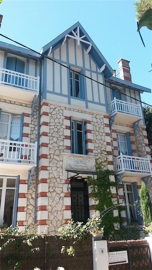 Een traditioneel huis met een mix van steen en houtwerk, gesitueerd in het hart van St. Palais sur Mer, Frankrijk, met duidelijke blauwe en witte kleuraccenten die schitteren onder een heldere hemel