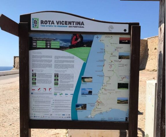 Een informatiebord over de wandelroute Rota Vicentina in het zuidwesten van Portugal. Het bord toont een kaart van de route door de regio's Alentejo en Algarve, met verschillende steden en bezienswaardigheden aangegeven. Er zijn ook pictogrammen en instructies voor wandelaars over hoe de route te volgen en wat ze onderweg kunnen verwachten