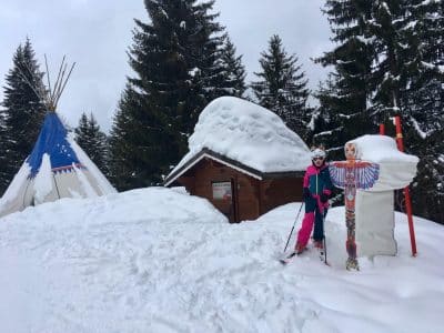 "Een persoon in skikleding naast een grote sneeuwpop en een tipi in het besneeuwde skigebied Portes du Soleil.