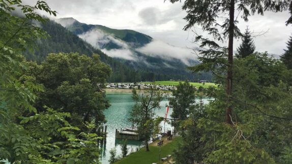 Een idyllisch uitzicht op de Achensee in Oostenrijk, met zijn helderblauwe water en omringende groene landschap, waar de laaghangende wolken zorgen voor een mystieke sfeer boven de glooiende heuvels en de rustige camping