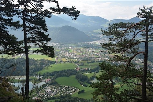 Uitzicht over Kramsach, Oostenrijk, gezien vanuit een bergpad met dennenbomen op de voorgrond en de Alpen op de achtergrond.