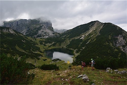 Twee wandelaars op een bergpad met een uitzicht op een mistig bergmeer en bergtoppen die de wolken raken