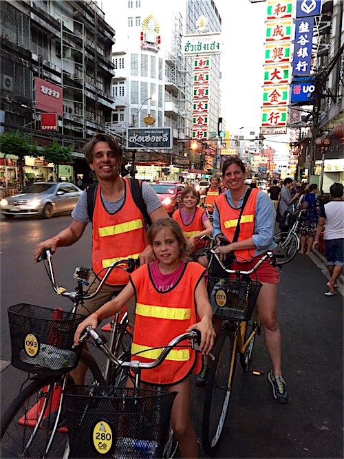 Een familie fietsend door een drukke straat in Bangkok, Thailand, gekleed in opvallende oranje veiligheidshesjes.